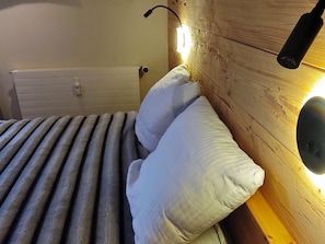 A bed with a wooden headboard and a wall-mounted light fixture. - Frostana 1600, (Champoussin), by Interhome (Champoussin)