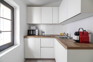 A compact kitchen with white cabinets, a microwave, a coffee maker, a red kettle, and a sink. - A/C studio in the heart of Cannes – Old Port (Cannes)