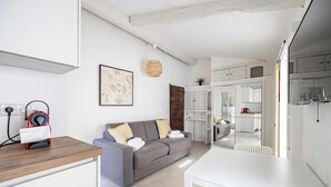Ein kompakter Wohnbereich mit grauem Sofa, weißem Tisch und einer Küchenzeile.
