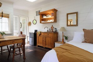 A cozy room with a bed, a wooden table, a refrigerator, a cabinet, and a mirror.