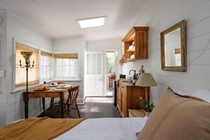A room with a bed, a table with chairs, a wooden cabinet, a mirror, and a window with blinds.