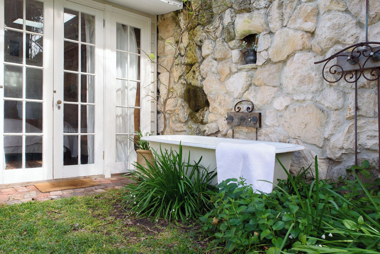 A stone wall with a rustic outdoor sink, a white door with glass panels, and a small garden area with green plants.