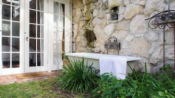A stone wall with a rustic outdoor sink, a white door with glass panels, and a small garden area with green plants.