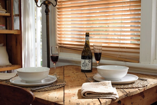A wooden dining table with two white bowls, a wine bottle, and two glasses of red wine.