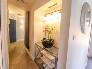 A hallway with a potted orchid plant on a glass console table, a wall-mounted mirror, and a ceiling fan. - Trefin (Cemaes Bay)