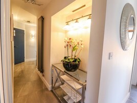 Un pasillo con una orquídea en maceta sobre una mesa consola de cristal, un espejo fijado a la pared y un ventilador de techo.