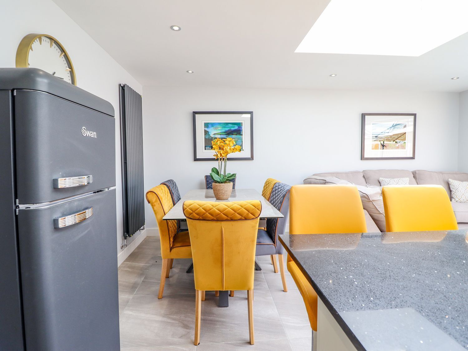 Una cocina moderna con un refrigerador gris, una mesa de comedor con sillas amarillas y una encimera gris.