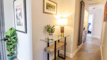 A hallway with a glass console table, a potted plant, a framed picture, and a lamp.