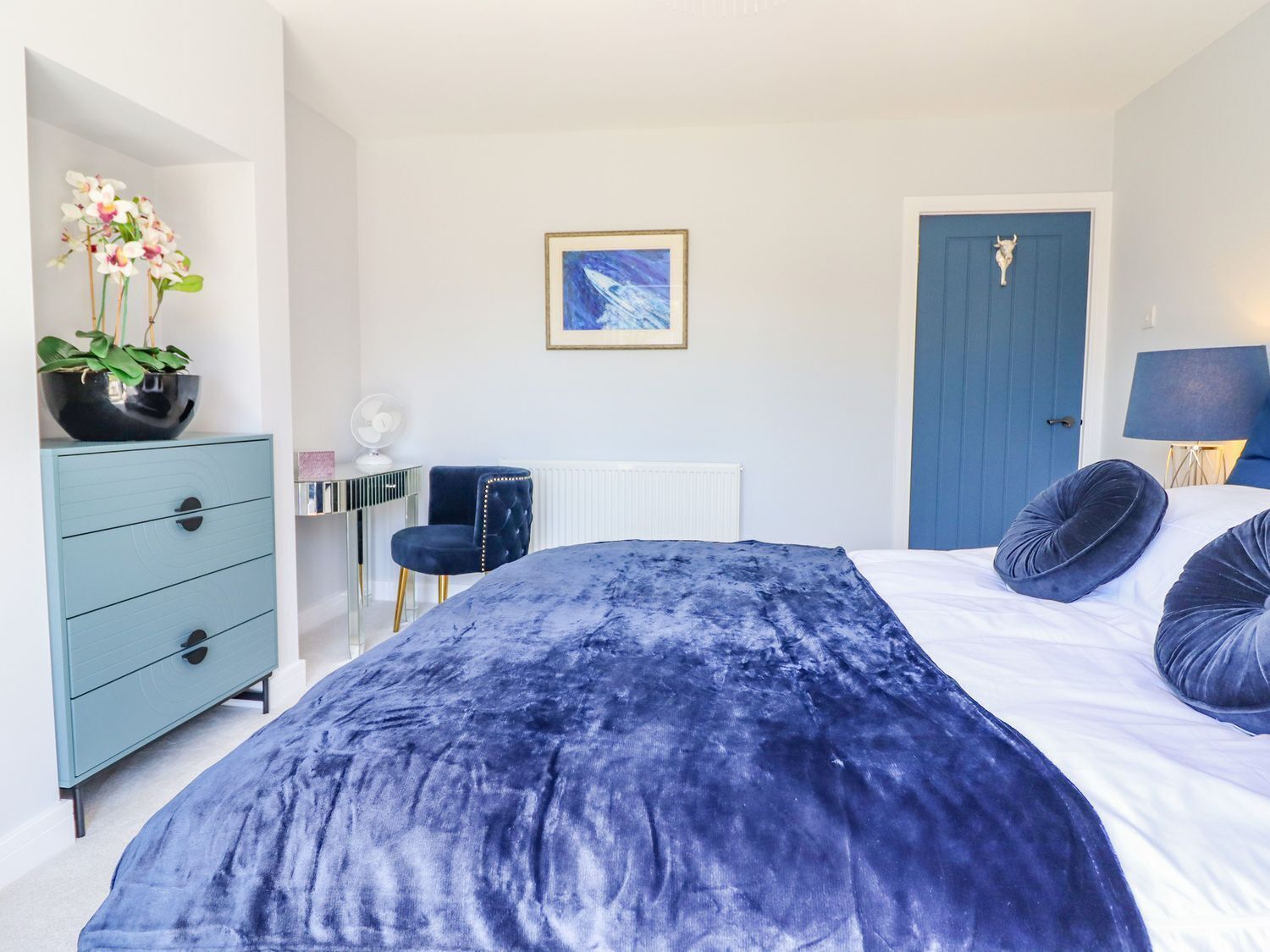Un dormitorio con cama, cómoda, silla, puerta y un cuadro en la pared.