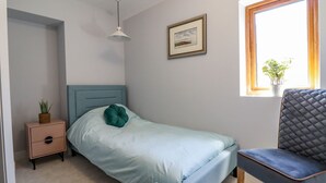 Ein Schlafzimmer mit Bett, Nachttisch, Stuhl, Fenster und einer Pendelleuchte.