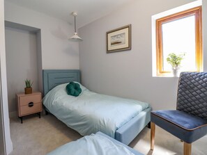 Ein Schlafzimmer mit Bett, Nachttisch, Stuhl, Fenster und einer Pendelleuchte.