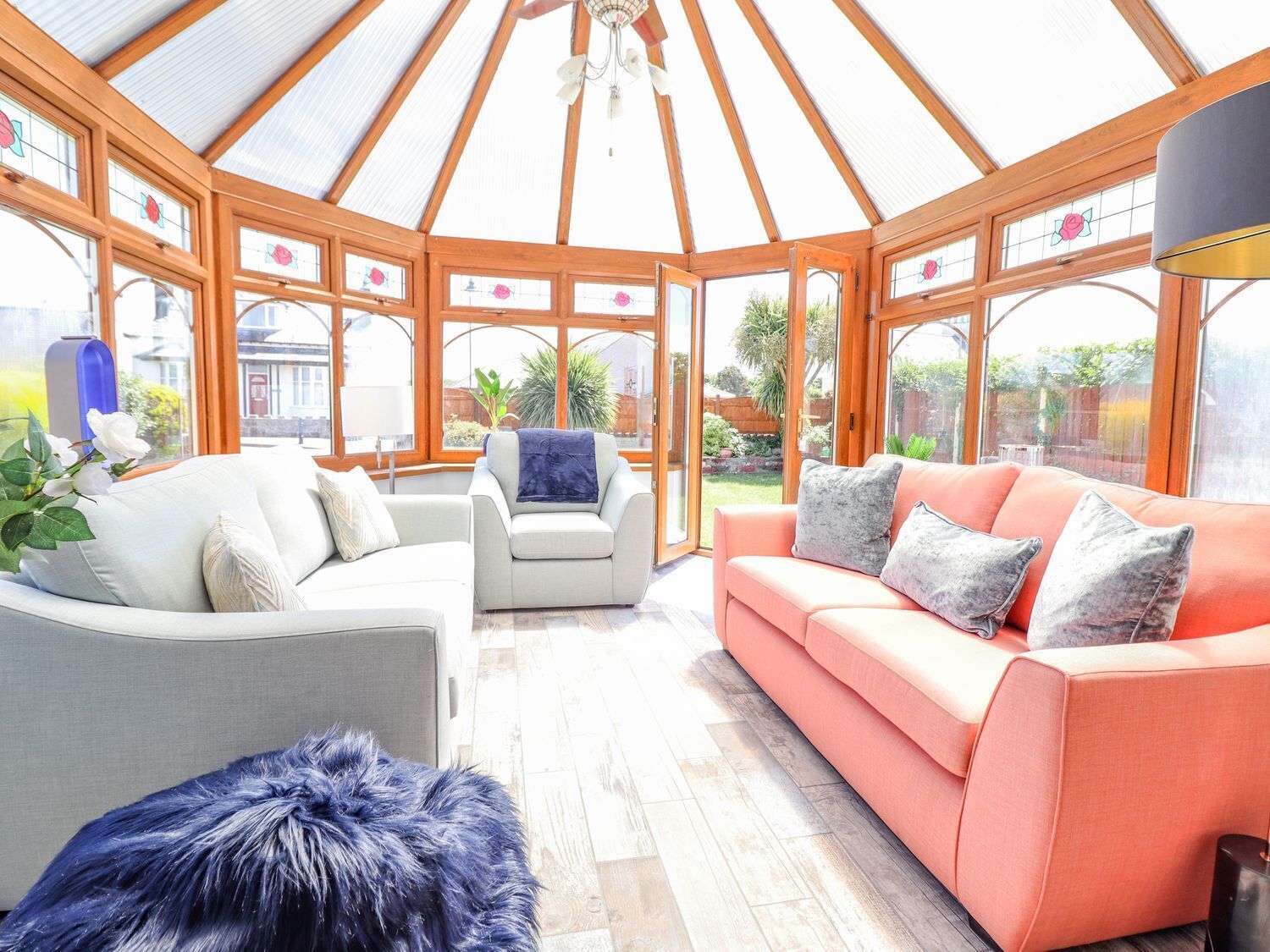 A conservatory with a wooden ceiling, large windows, and a seating area with sofas and a furry rug.