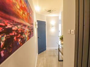 A hallway with a blue door, a ceiling fan, and a painting on the wall.