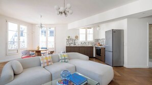 A modern living room with a sofa, a glass coffee table, and a kitchen area with a refrigerator and stove. - Bright and Spacious 1BDR in Central Paris (Paris)