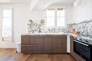 A kitchen with a marble backsplash, wooden cabinets, and a built-in oven. - Bright and Spacious 1BDR in Central Paris (Paris)