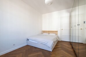 Ett sovrum med en säng, trägolv, vita väggar och en garderob med glasdörrar.