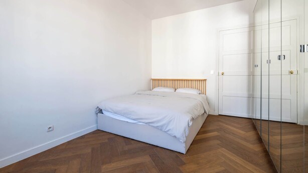 A bedroom with a bed, wooden floor, white walls, and a wardrobe with glass doors. - Bright and Spacious 1BDR in Central Paris (Paris)