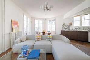 Ein modernes Wohnzimmer mit einer Eckcouch, einem Glastisch und Blick auf die Stadt durch große Fenster.
