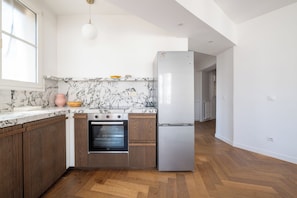 Eine moderne Küche mit Marmorarbeitsplatten, Holzschränken, einem Edelstahlbackofen und einem Kühlschrank.