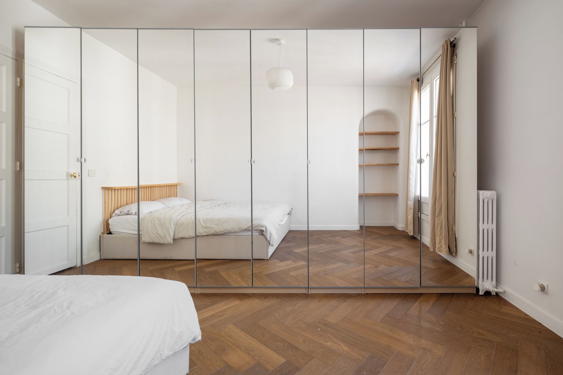 Une chambre à coucher avec un lit, une armoire, un radiateur et une fenêtre avec des rideaux.