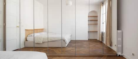 Une chambre à coucher avec un lit, une armoire, un radiateur et une fenêtre avec des rideaux.