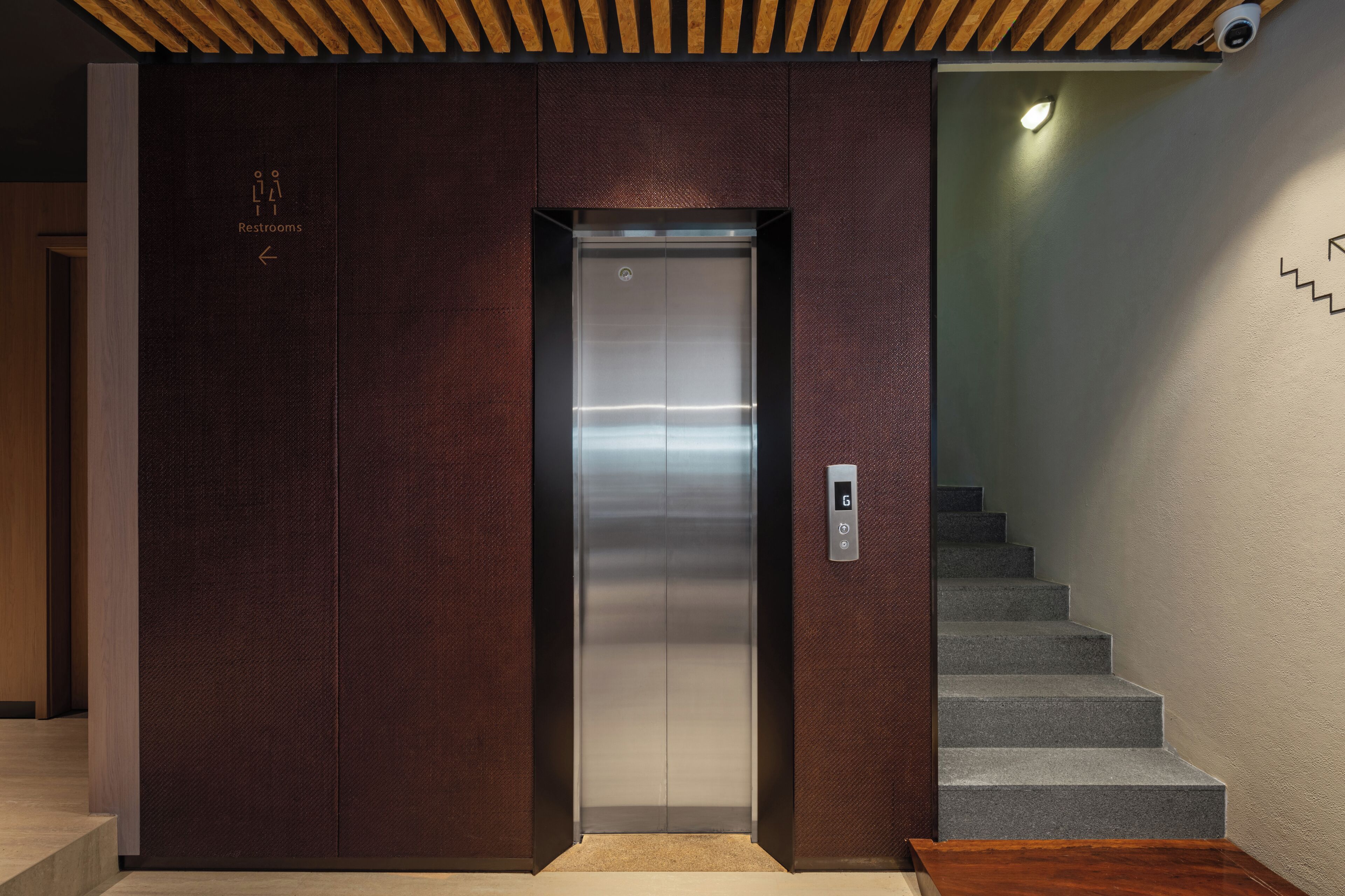 An elevator with a metallic interior, a control panel with a 'G' button, and a staircase to the right.