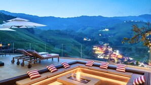 Una terraza en la azotea con un brasero, asientos tipo lounge y vistas a un valle con luces a lo lejos.