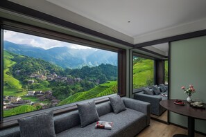 Ein modernes Interieur mit einem großen Fenster, das einen Blick auf eine von Terrassen durchzogene Landschaft und ein Dorf bietet.