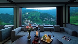 Una habitación moderna con un ventanal grande que da a un valle verde y un pueblo.