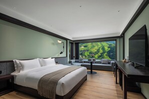 A modern hotel room with a large bed, a sofa, a dining table, and a TV.