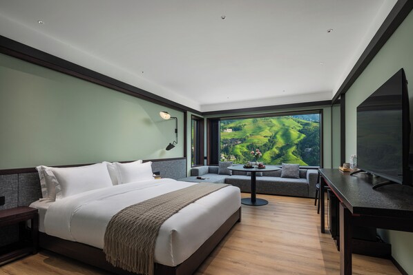 A modern hotel room with a large bed, a sofa, a dining table, and a TV.