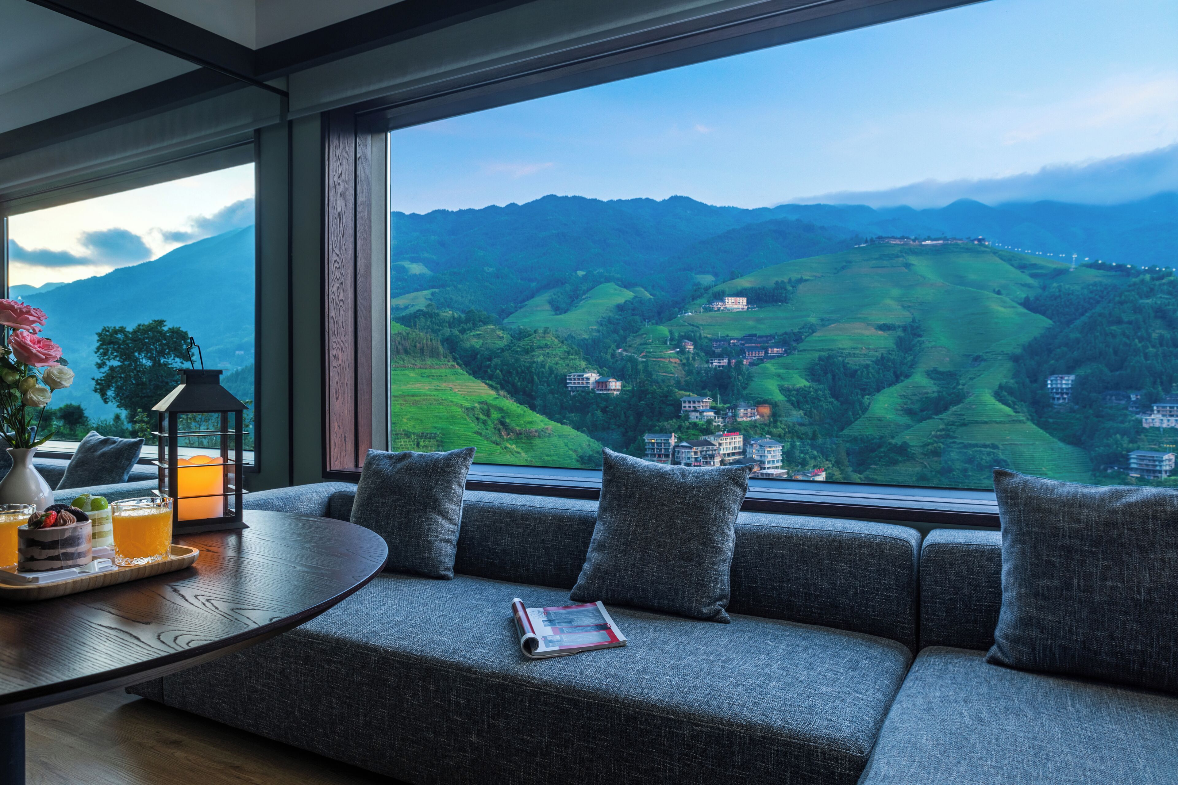 A modern room with a large window offering a view of green hills and buildings.