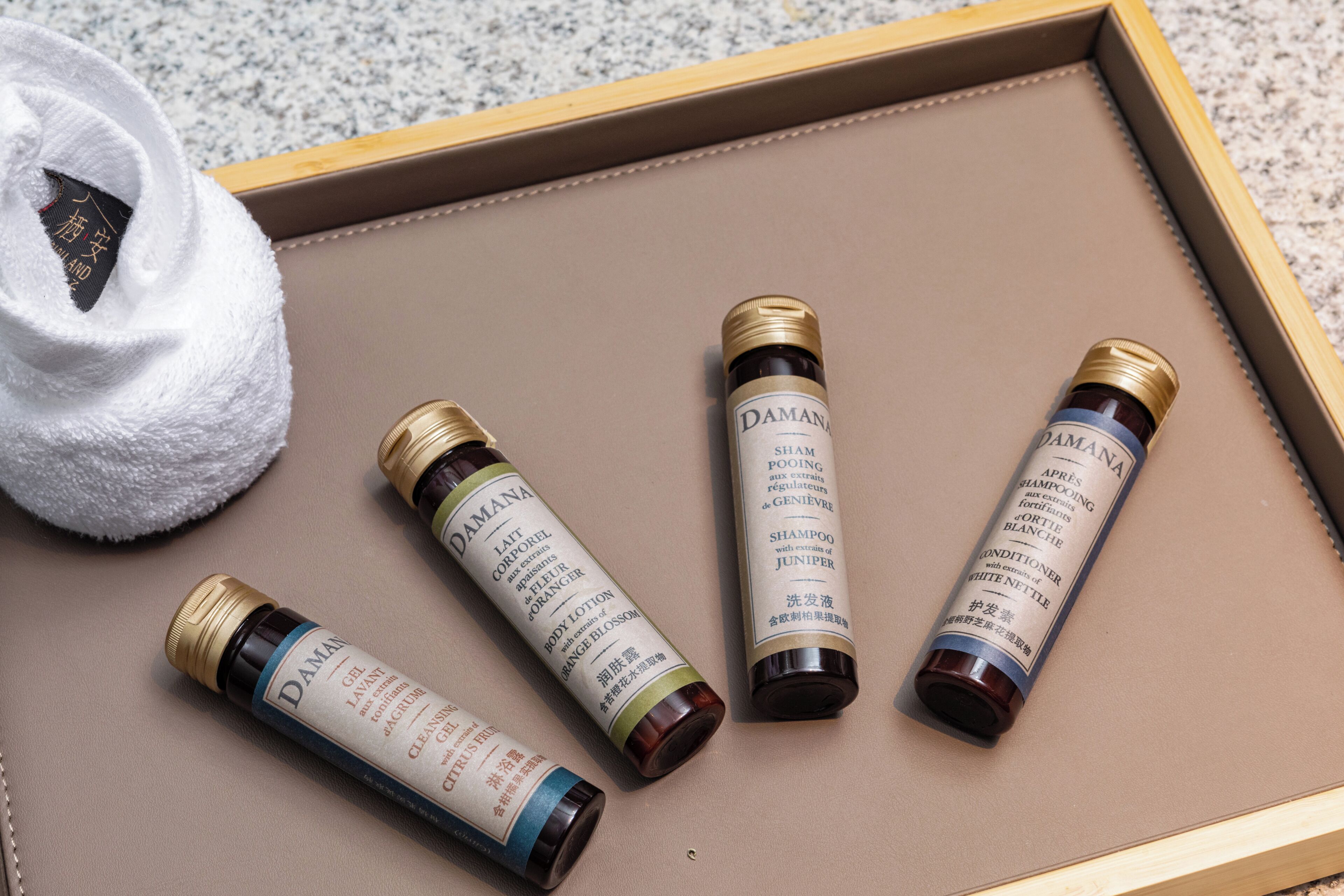 Un vassoio con quattro bottiglie di shampoo Damana, un asciugamano bianco e un vassoio di legno.