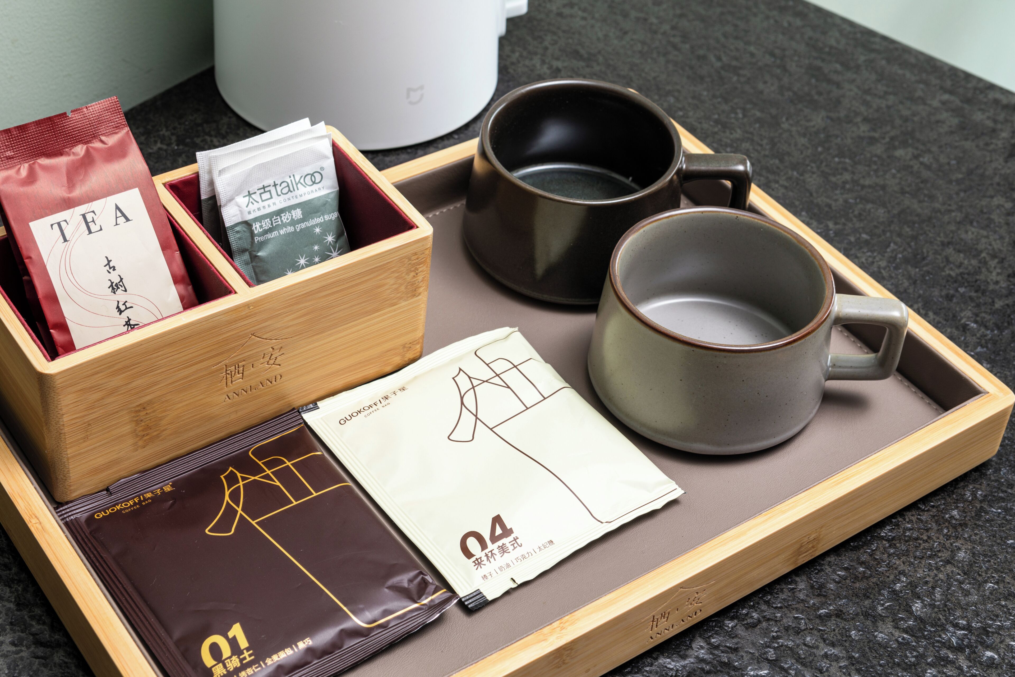 A tray with tea bags, a coffee bag, a mug, and a box labeled 'ANNLAND'.