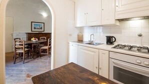 Une cuisine avec des meubles blancs, une cuisinière à gaz, un évier et un coin repas comprenant des chaises et une table en bois.