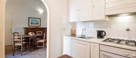 A kitchen with white cabinets, a gas stove, a sink, and a dining area with wooden chairs and a table.