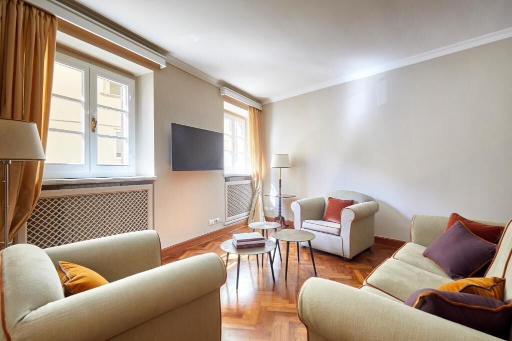 A living room with a sofa, armchairs, a coffee table, and a flat-screen TV mounted on the wall.