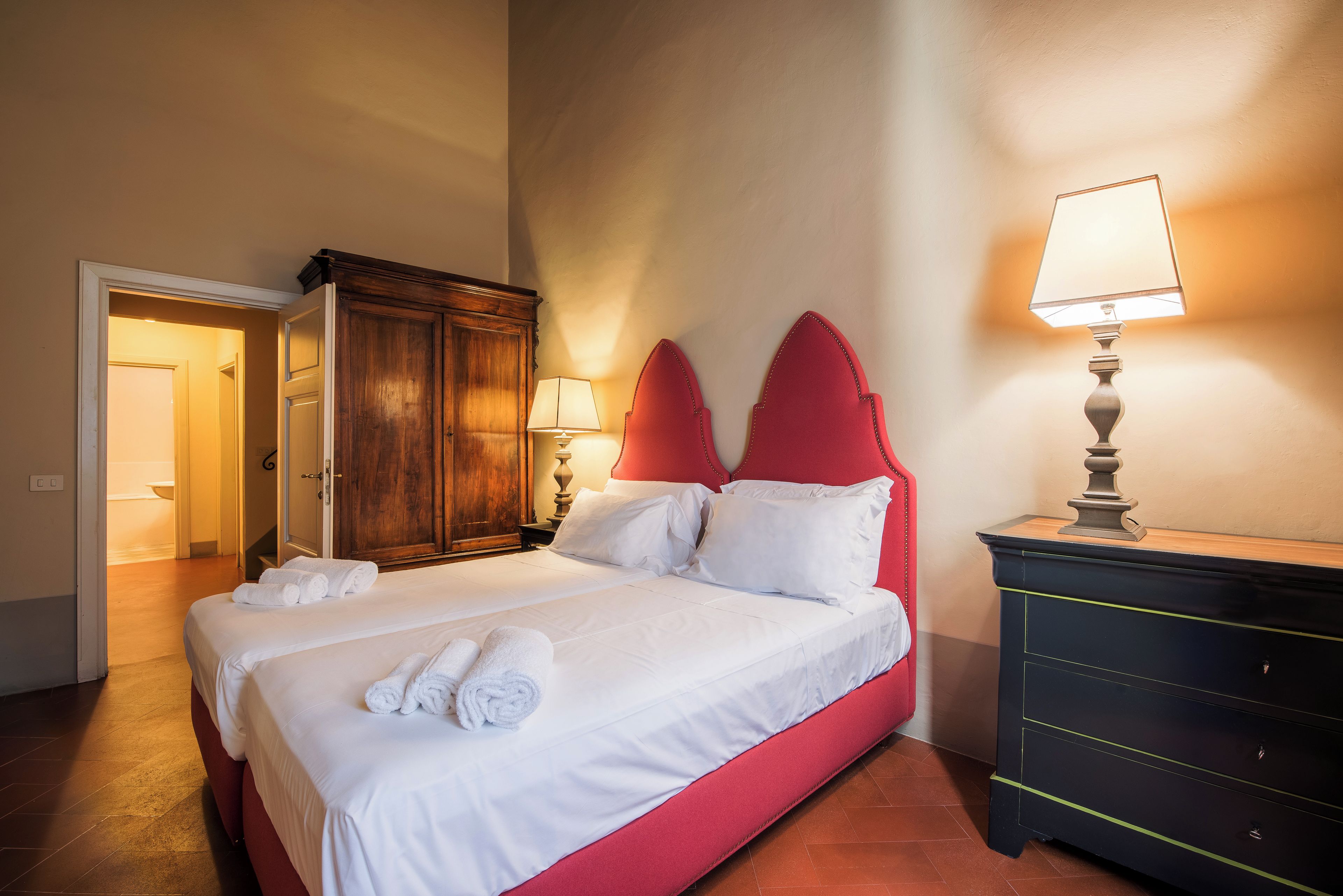 A hotel room with a bed, a wardrobe, a nightstand, and a lamp.