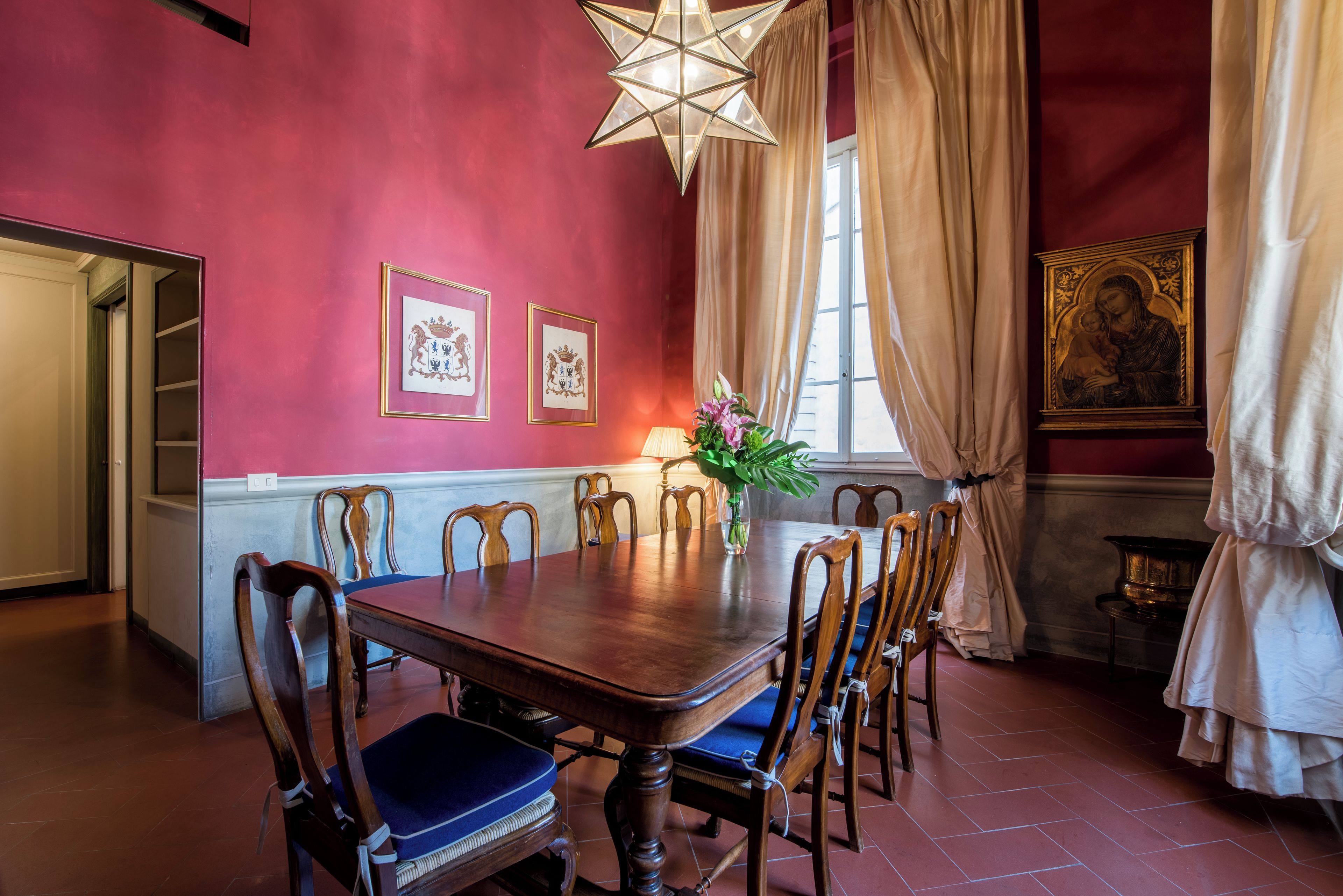 A dining room with a wooden table, chairs, a chandelier, and framed artwork on the walls.