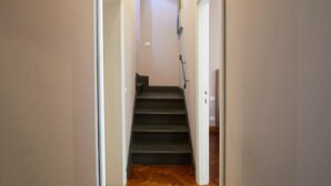 Un couloir étroit, doté d’un plancher en bois, qui mène à un escalier.