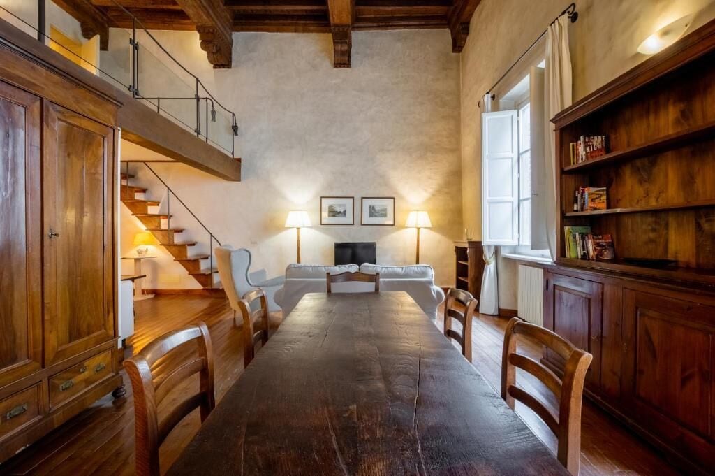 Ein geräumiger Essbereich mit einem langen Holztisch, umgeben von Stühlen, einer Treppe und einem Bücherregal.