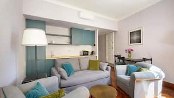 A modern living space with a sofa, armchairs, a small round table, and a kitchenette area.