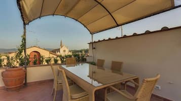 An outdoor patio with a glass-top table and wicker chairs, overlooking a cityscape with a church.
