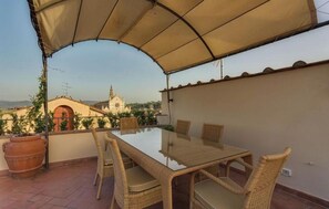 An outdoor patio with a glass-top table and wicker chairs, overlooking a cityscape with a church.