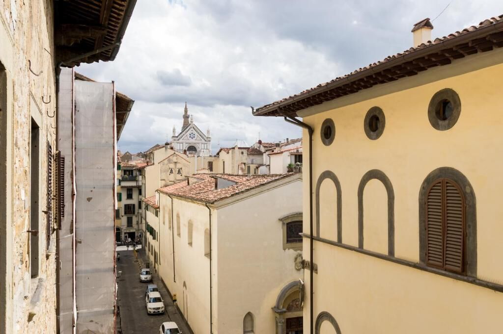 Una calle estrecha flanqueada por edificios, una iglesia con un campanario a lo lejos, y un cielo despejado.