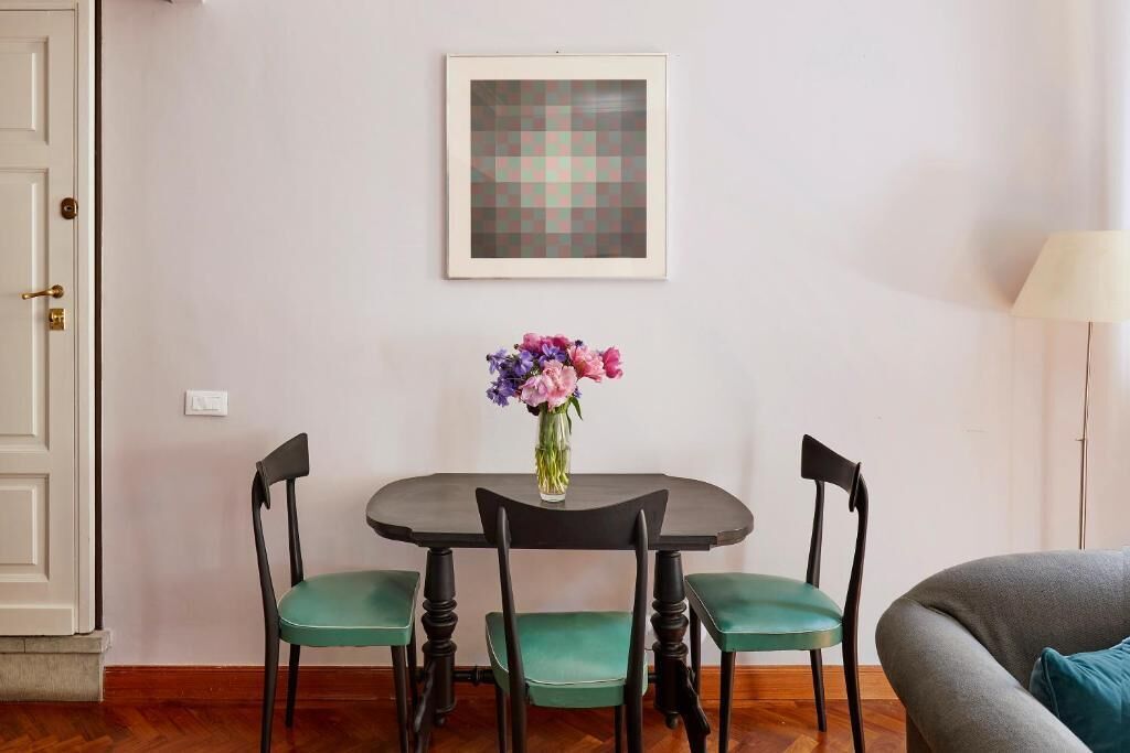 Ein Essbereich mit Tisch, Stühlen, einem Blumenstrauß und einem gerahmten Bild an der Wand.