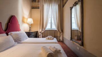 A hotel room with two beds, a nightstand, a lamp, a mirror, and a window with curtains.