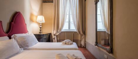 Habitación de hotel con dos camas, una mesita de noche, una lámpara, un espejo y una ventana con cortinas.