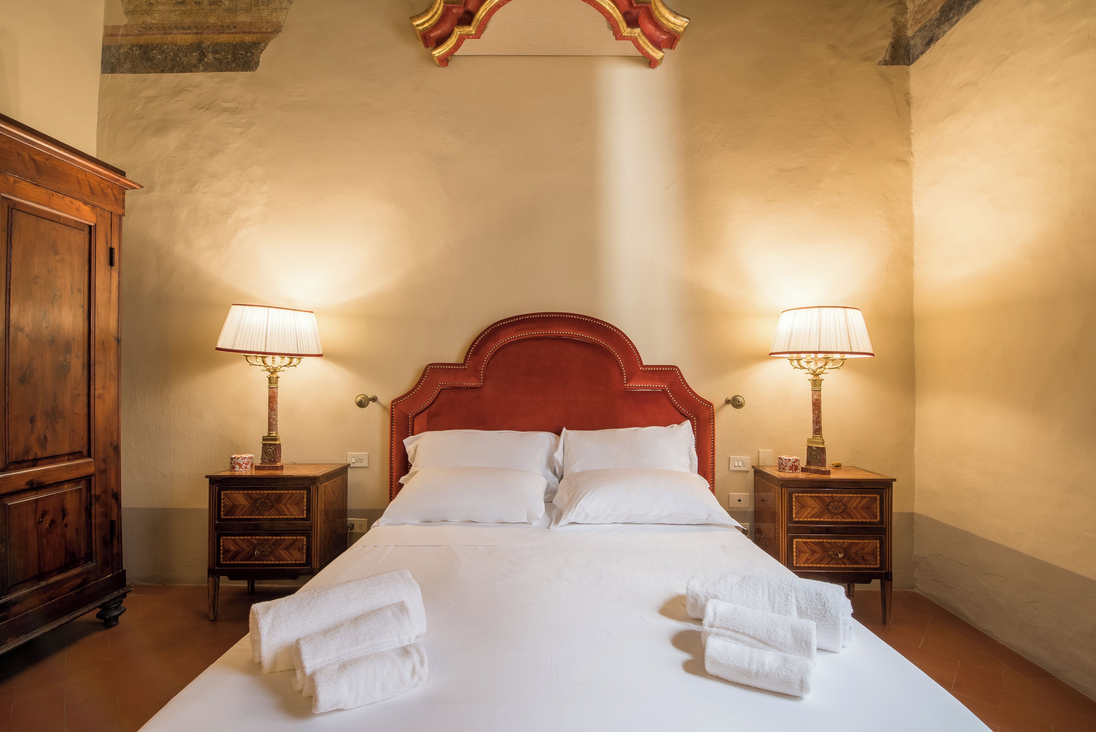 A hotel room with a large bed, two bedside tables with lamps, a wooden wardrobe, and a decorative ceiling piece.