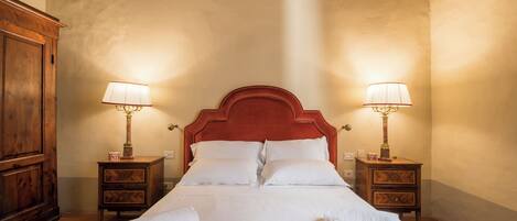 A hotel room with a large bed, two bedside tables with lamps, a wooden wardrobe, and a decorative ceiling piece.